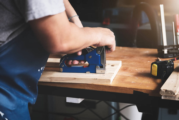 Unternehmer Woodwork hält einen Tacker in der Hand, um die Holzteile nach Kundenwunsch zu montieren. - Foto, Bild