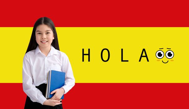 Kleine asiatische Schülerin und Wort HOLA (HELLO) gegen Flagge Spaniens - Foto, Bild