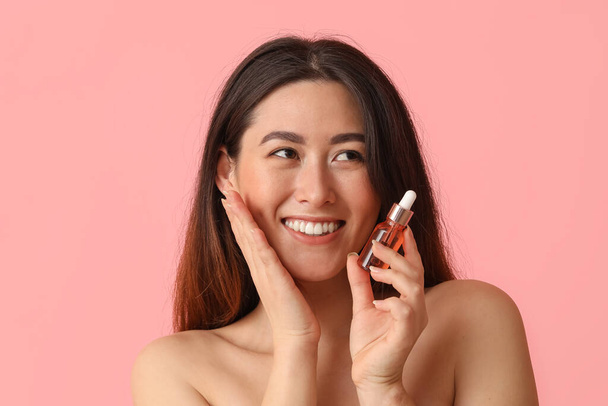 jong aziatisch vrouw met cosmetisch serum op roze achtergrond - Foto, afbeelding