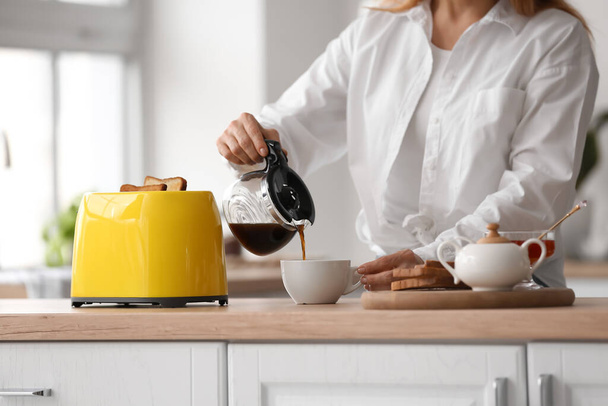 Mature woman making tasty toasts and drinking coffee in kitchen - Foto, Bild