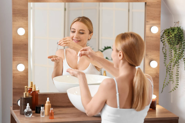 Зріла жінка використовує косметичну сироватку у ванній
 - Фото, зображення