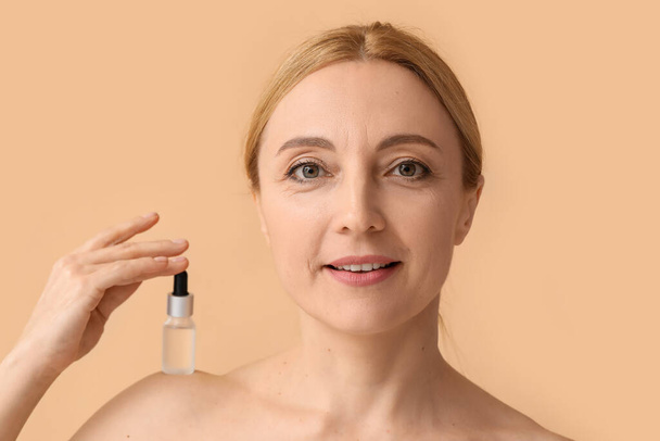 Dojrzała kobieta z kosmetycznym serum na beżowym tle - Zdjęcie, obraz