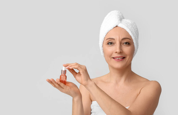 Mature woman with cosmetic serum on light background - Photo, Image