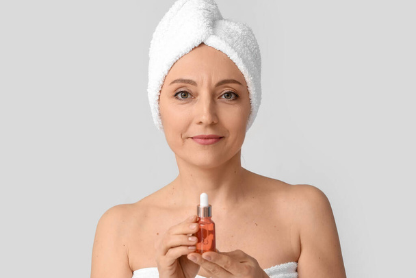 Mujer madura con suero cosmético sobre fondo claro - Foto, imagen