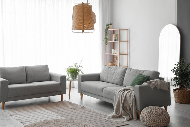 Interior of light living room with grey sofas, shelving unit and houseplants - Foto, afbeelding