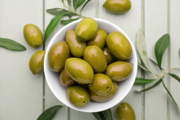 Bowl of green olives on light wooden background, closeup - Foto, imagen