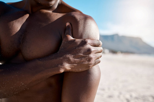 Closeup shot of an african american muscular athletic man holding his shoulder in pain. Black unrecognizable male suffering from arthritis in his arm. Suffering from a hurting, stiff, injured joint. - Fotografie, Obrázek