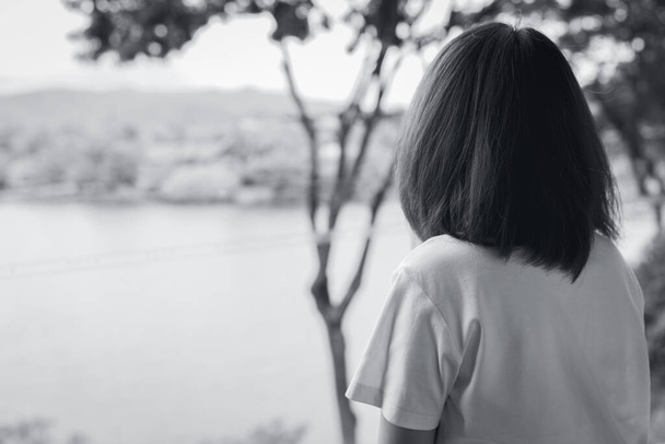 Back view of sad Asian woman in the park look the view of lake. Depressed woman. Mental health concept. Worry and anxiety woman. Unhappy life. Alone and lonely person. Black and white photography. - Foto, Imagem