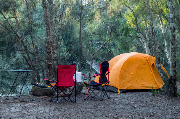 Pomarańczowy namiot na brzegu rzeki w lesie. Turystyka turystyczna camping koncepcja życia - Zdjęcie, obraz