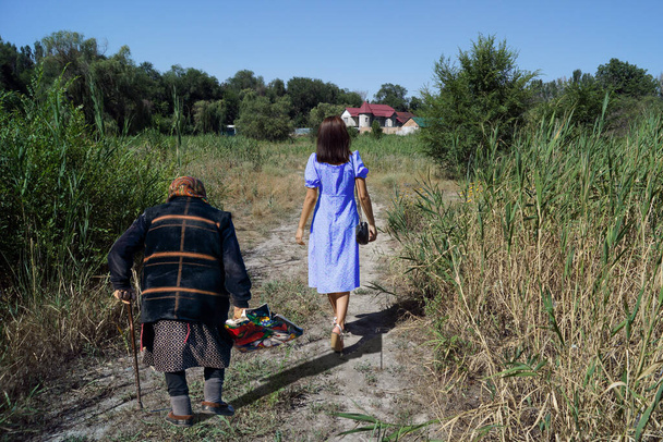 A lonely young girl walking along a reed path, and a grandmother walking behind her. - Photo, Image