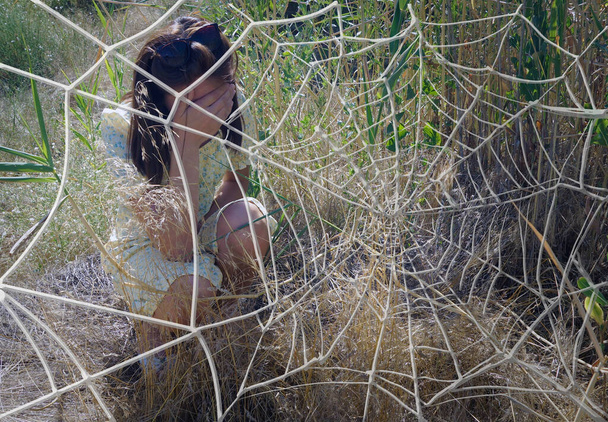 An offended, angry girl is sitting behind a web in the reeds. - Fotoğraf, Görsel