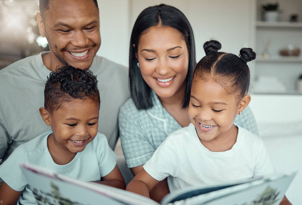 Junge Eltern gemischter Rassen lesen ihren Töchtern und Söhnen ein Buch vor, während sie morgens zu Hause Zeit miteinander verbringen. Zwei Kinder genießen Märchengeschichte im Sitzen - Foto, Bild