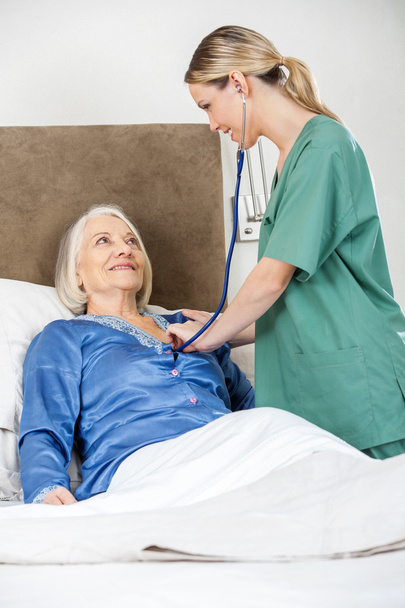 Huoltaja tutkii vanhempi nainen kanssa stetoskooppi makuuhuoneessa
 - Valokuva, kuva