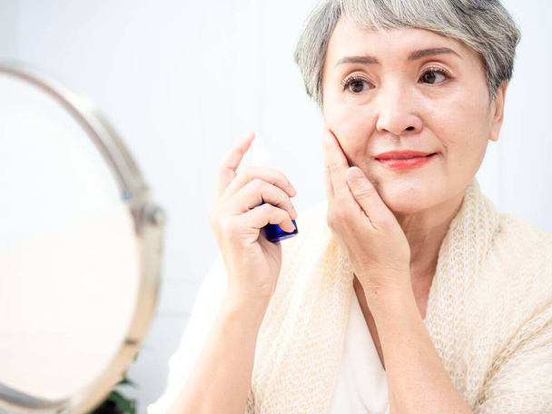 Portrait of mature aged asian woman 60s sprays perfume. - Valokuva, kuva