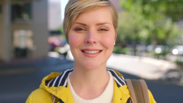 Portrait of a beautiful smiling woman looking happy outside. Face closeup of a young trendy female enjoying exploring and laughing in the city street. Headshot of a cheerful tourist with blonde hair. - Filmagem, Vídeo