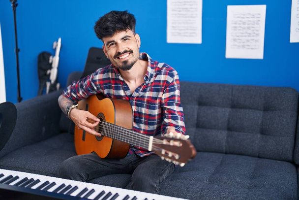 Young hispanic man artist smiling confident playing classical guitar at music studio - Foto, Imagem