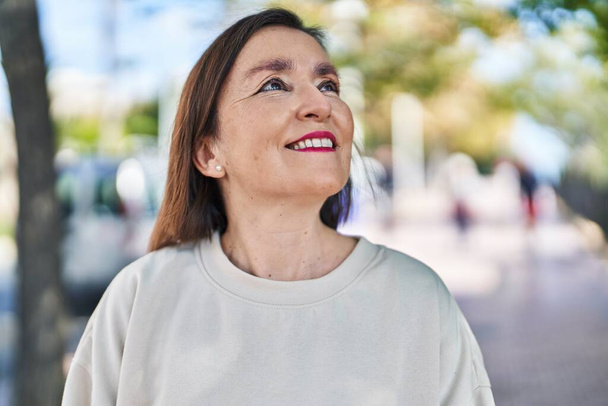 Жінка середнього віку посміхається впевнено дивлячись в небо в парку
 - Фото, зображення