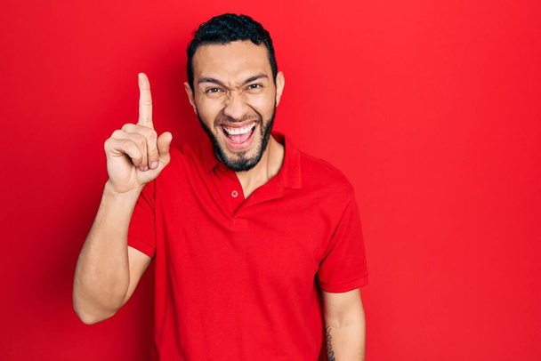 髭を生やしたヒスパニック系の男性は、成功したアイデアで指を指してカジュアルな赤いTシャツを着ていた。興奮して幸せよ。第1位.  - 写真・画像