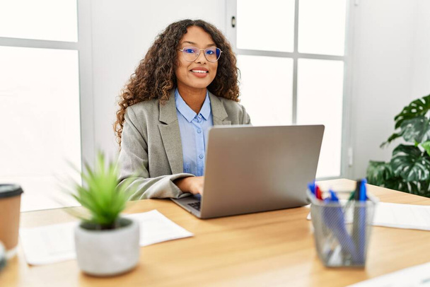 Молодая латиноамериканка уверенно улыбается, работая в офисе - Фото, изображение