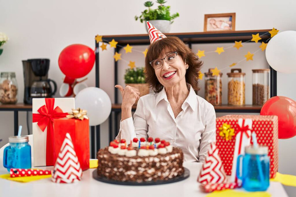 Жінка середнього віку, яка святкує день народження, тримає великий шоколадний торт, спрямований на великий палець до сторони, посміхаючись щасливим з відкритим ротом
  - Фото, зображення