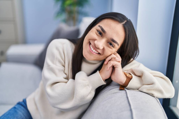 Mladá hispánka se usmívá sebevědomě sedí na pohovce doma - Fotografie, Obrázek