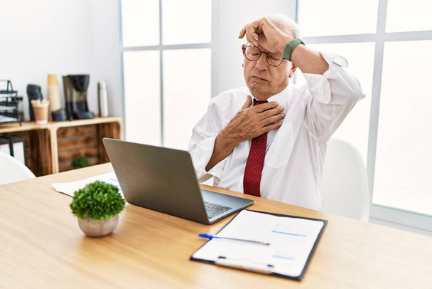 Senior man working at the office using computer laptop touching forehead for illness and fever, flu and cold, virus sick  - Fotó, kép