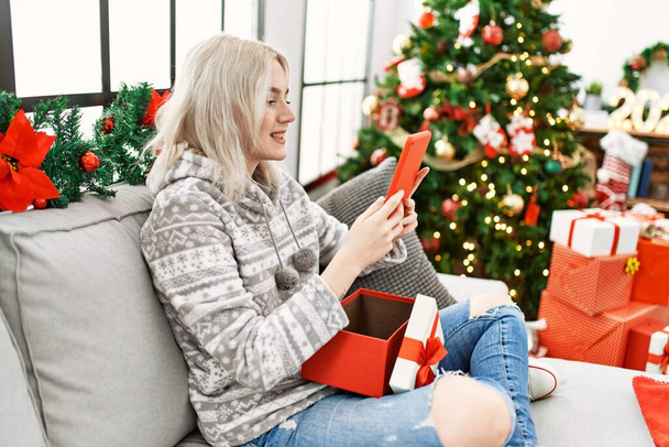 Young caucasian girl smiling happy holding touchpad christmas gift at home. - 写真・画像