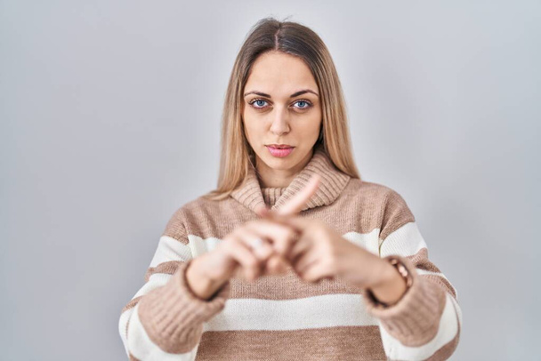 Молода блондинка в светрі з черепашками над ізольованим фоном вираз відторгнення схрещування пальців робить негативний знак
  - Фото, зображення