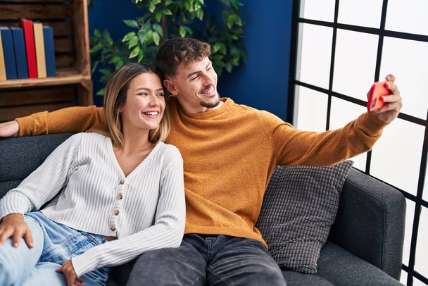 Young man and woman couple make selfie by the smartphone sitting on sofa at home - Foto, imagen