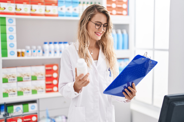 Young woman pharmacist reading report holding pills bottle at pharmacy - Foto, immagini