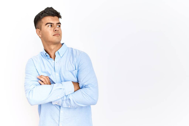 Giovane uomo ispanico indossa business shirt in piedi su sfondo isolato guardando a lato con le braccia incrociate convinto e fiducioso  - Foto, immagini
