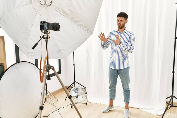 Arabischer junger Mann, der als Model im Fotostudio posiert und Handflächen wegbewegt, die Verweigerung und Verleugnung mit ängstlichem und ekelhaftem Ausdruck zeigen. Stopp und Verbot.  - Foto, Bild