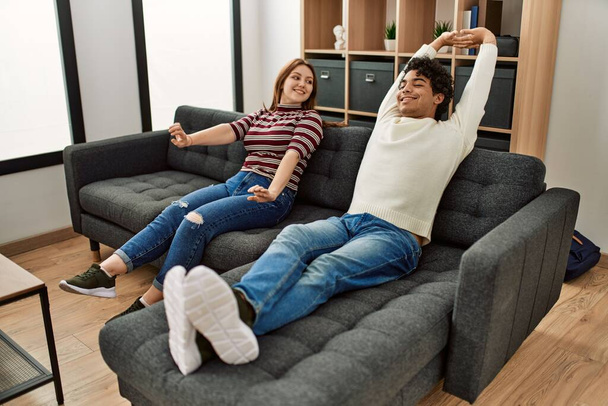 Junges Paar lächelt glücklich entspannt auf dem heimischen Sofa sitzend. - Foto, Bild