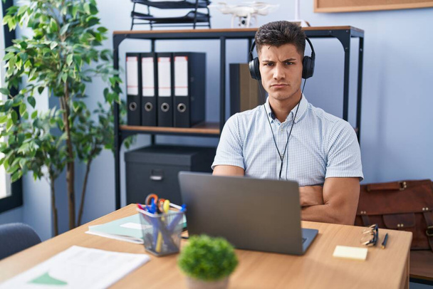 Young hispanic man working at the office wearing headphones skeptic and nervous, disapproving expression on face with crossed arms. negative person.  - Фото, зображення