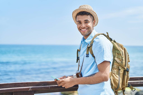 African american man tourist smiling confident using smartphone at seaside - Photo, Image