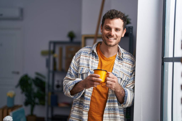 Young hispanic man artist drinking coffee standing at art studio - Valokuva, kuva