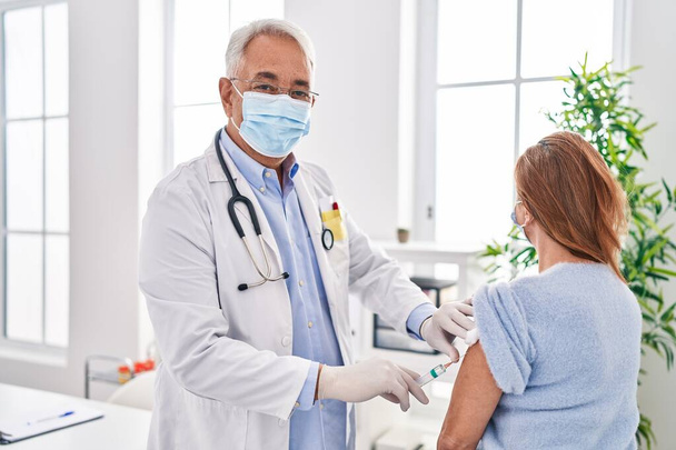 Médico y médico de mediana edad con máscara médica vacunando al paciente en la clínica - Foto, imagen