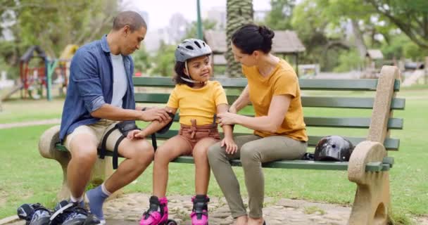 Caring parents making sure their daughter is safe and protected while rollerskating at a public park. Cute little adopted girl wearing protective gear and rollerskates while having fun outdoors. - Кадри, відео