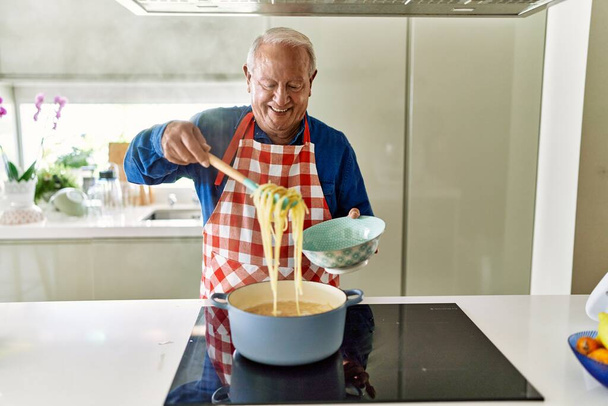 Uomo anziano sorridente spaghetti di cucina fiducioso in cucina - Foto, immagini