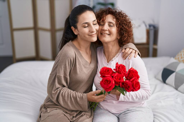 Two women mother and daughter hugging each other holding bouquet of flowers  - Foto, imagen