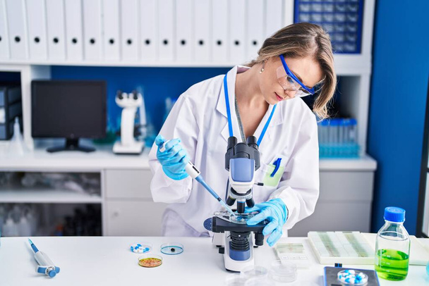 Young woman scientist pouring liquid on sample using microscope at laboratory - Photo, image