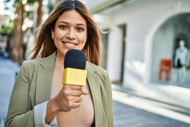 Mladá latinská žena s úsměvem sebevědomě pomocí mikrofonu na ulici - Fotografie, Obrázek