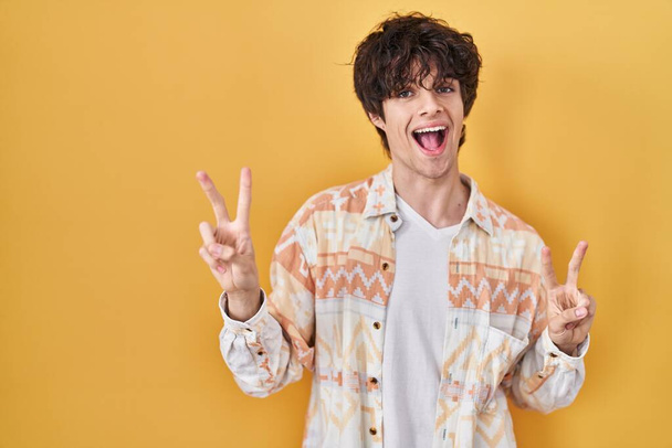 Young man wearing casual summer shirt smiling looking to the camera showing fingers doing victory sign. number two.  - Foto, Imagen