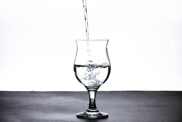 Изображение наливания питьевой воды в стакан, который освежает ощущение свежести на размытом белом фоне - Фото, изображение