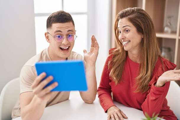 Mother and son using touchpad device celebrating achievement with happy smile and winner expression with raised hand  - Foto, Bild
