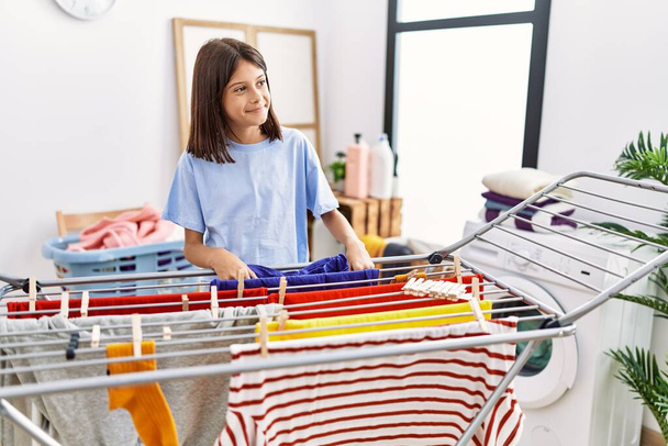 Junges hispanisches Mädchen hängt Wäsche an Wäscheleine in Waschküche - Foto, Bild