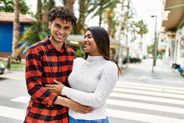 Joven pareja latina sonriendo feliz y abrazándose a la ciudad. - Foto, imagen