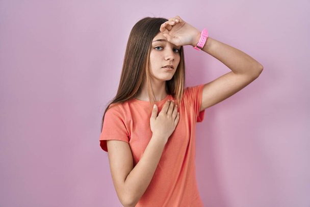 Дівчинка-підліток стоїть над рожевим тлом торкаючись лоба за хворобу і гарячку, грип і холод, вірус хворіє
  - Фото, зображення