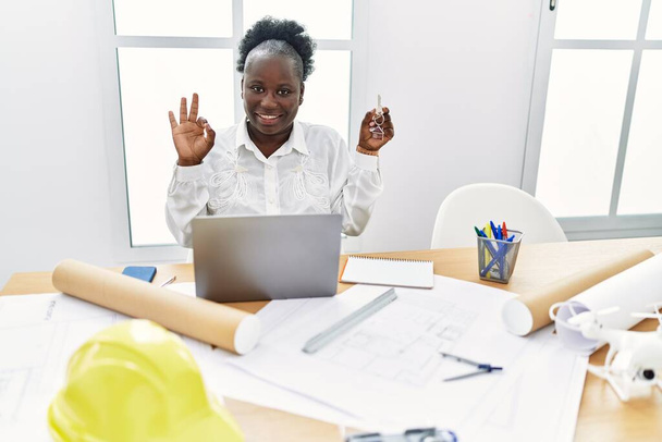 Jovem mulher africana trabalhando no estúdio de arquitetura segurando as teclas da casa fazendo sinal ok com os dedos, sorrindo amigável gesto excelente símbolo  - Foto, Imagem