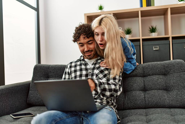 Jeune couple utilisant un ordinateur portable assis sur le canapé à la maison. - Photo, image